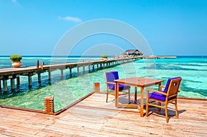 Tables and chairs in a wooden restaurant on stilts on the background of azure water and blue sky