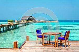 Tables and chairs in a wooden restaurant on stilts on the background of azure water and blue sky