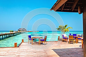 Tables and chairs in a wooden restaurant on stilts on the background of azure water and blue sky