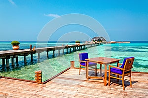 Tables and chairs in a wooden restaurant on stilts on the background of azure water and sunny sky