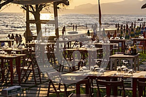 Tables in outdoor cafe or restaurant served for dinner on crowded beach with sea view, summer holidays