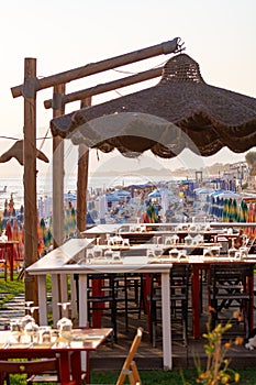 Tables in outdoor cafe or restaurant served for dinner on crowded beach with sea view, summer holidays