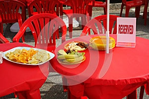 Tables under a red tablecloth with dishes of crisps, fruit and a reserved sign.