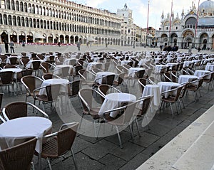 Tables waiting for tourists in nearly vacant St. Mark`s Square Venice Italy