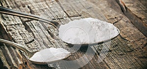 Tablespoon and teaspoon with baking soda, on wooden background. Close up view.