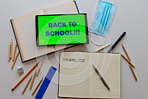 Tablet with `back to school` text, book, template, notebook, pens, pencils on white surface. Back to school and beginning of the s