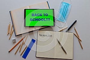 Tablet with `back to school` text, book, template, notebook, pens, pencils on white surface. Back to school and beginning of the s