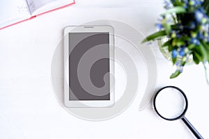 Tablet with black empty screen. Notebook, magnifier and flowers on table