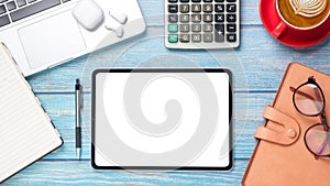 Tablet with blank screen, laptop computer, calculator, notebook, eyeglass, pen and cup of coffee on wooden desk.