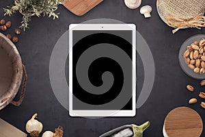 Tablet with blank screen on old country kitchen table surrounded with meal ingredients and kitchen items