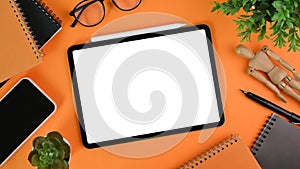 Tablet with blank screen, smart phone, house plant ,glasses and notebook orange background.