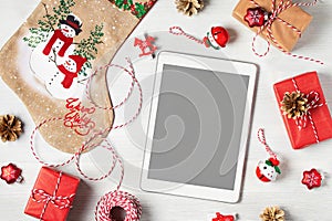 Tablet with a blank screen surrounded by Christmas decorations and gifts, mockup for advertising