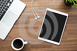 Tablet with blank screen is on top of wood office desk table with computer laptop and coffee. Top view, flat lay