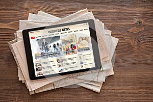 Tablet with business news website on stack of newspapers. All contents are made up.