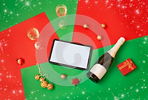 Tablet, champagne, christmas decorations and gift on colorful background