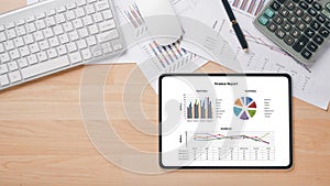 Tablet with charts and reports, pen, calculator, notebook, mouse and keyboard on office desk workplace.