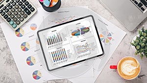 Tablet with charts and reports, pen, calculator, notebook, mouse and keyboard on office desk workplace.