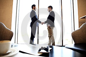 Tablet computer, coffee and smartphone with businessmen handshaking on background