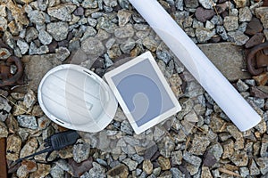 A tablet computer, hardhat, walkie-talkie and train route chart lie on ballast stone in railroad next to railroad sleeper and rail