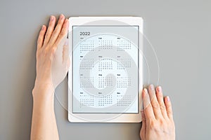 Tablet computer with an open app of calendar for 2022 year in a womans hands on a gray background. concept business or to do list