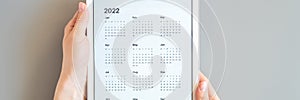 tablet computer with an open app of calendar for 2022 year in a womans hands on a gray background. concept business or to do list