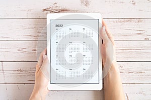 tablet computer with an open app of calendar for 2022 year in a womans hands on a wooden boards background. concept business or to