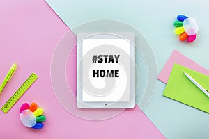 Tablet computer with stayhome hashtag, pen, ruler and colorful markers on pink and blue background