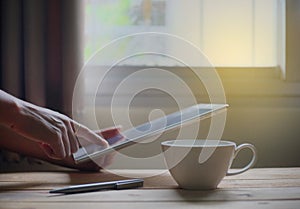 Tablet and a cup of coffee on wood table window background . working at home.