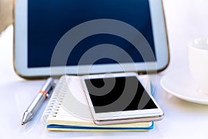 Tablet with a cup and smartphone on the white table.