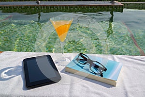 Tablet with empty screen, a glass of orange juice and blue book with glasses on the white towel