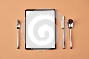 Tablet, fork, knife and spoon lying isolated on beige background, conceptual photography for food blog or advertising