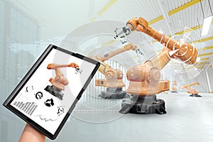 A tablet in a man`s hand controlling robotic arms in a modern factory. Iot technology concept, smart factory. Digital