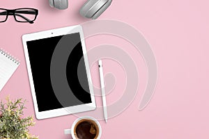 Tablet mockup on pink work desk surrounded with headphones, glasses, notepad, plant, cup of coffee and pen