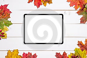 Tablet mockup on white wooden table surrounded by autumn leaves