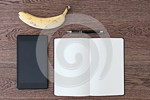 Tablet, notebook, pen and a banana on a wooden table. Image concept for journalism, liar and fake news, problems of hoaxes and tr