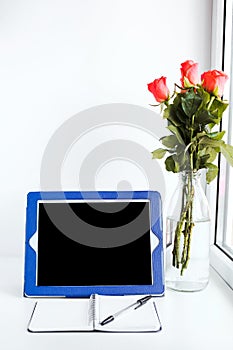 Tablet, notepad and a bouquet of flowers on the desktop by the window,