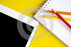 Tablet and notepad with color pencils on the yellow background.