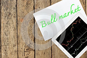 Tablet and paper with text bull market on wood table