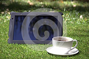 Tablet pc and a cup of coffee on the grass