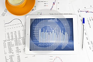 Tablet pc, cup of coffee and paper with graphs