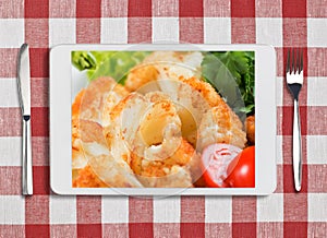 Tablet pc with dish, fork and knife on red checked tablecloth