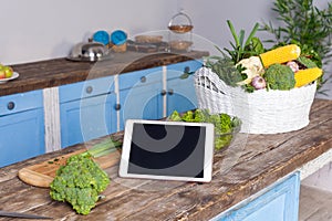 Tablet pc, fresh vegetables and cooked salad on wooden table in modern kitchen, concept of online cooking tips