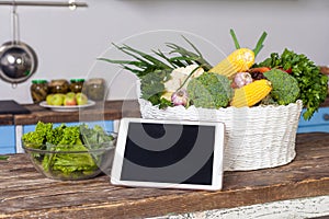 Tablet pc, fresh vegetables and cooked salad on wooden table in modern kitchen, concept of online cooking tips