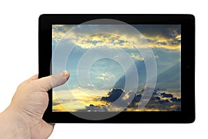 Tablet PC in hand with beautiful blue sky with golden sunset background on screen isolated