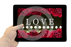 Tablet PC in hand with frame with love card with bush of red rose flowers and play of light on defocusing blur led lamps