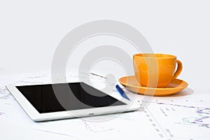 Tablet pc, orange cup and paper with graphs