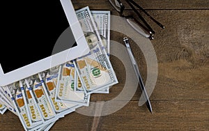 Tablet pc with a pen, glasses and dollar bills on a wooden table top view