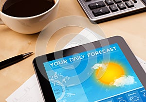 Tablet pc showing weather forecast on screen with a cup of coffee on a desk