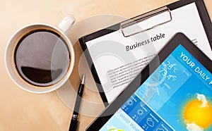 Tablet pc showing weather forecast on screen with a cup of coffee on a desk