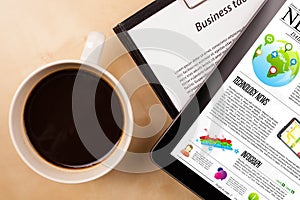 Tablet pc shows news on screen with a cup of coffee on a desk